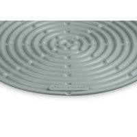 Tapis circulaire vert clair à motif spiralé, en matériau synthétique, avec logo LE CREUSET.