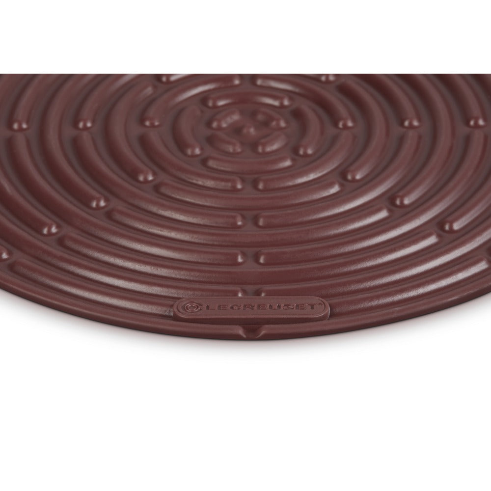 Tapis rond marron à surface spiralée, en silicone, avec logo "LE CREUSET" visible sur le bord.