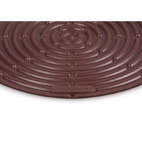 Tapis rond marron à surface spiralée, en silicone, avec logo "LE CREUSET" visible sur le bord.