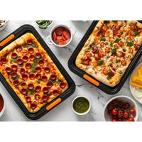 Two pizza pans, one with red pepper and pesto, the other with cherry tomatoes and mushrooms, surrounded by sauce, tomatoes and fresh ingredients.