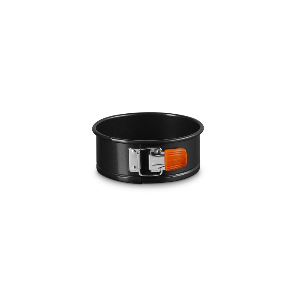 Black metal round baking pan with side clasp and orange handle. White background.