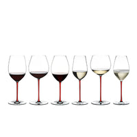 Seis copas de vidrio transparente con tallo rojo, con vino tinto, blanco y espumoso, alineadas sobre fondo blanco.