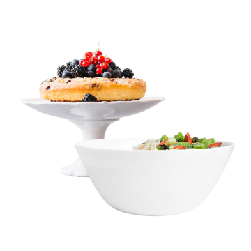 Torta rotonda con glassa bianca e frutti di bosco freschi su alzata, accanto a ciotola bianca con insalata