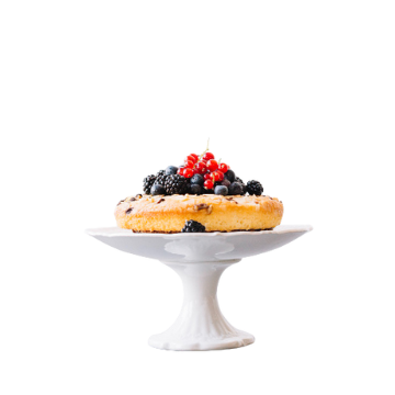 Torta rotonda gialla con frutti di bosco neri e rossi su alzata bianca in ceramica, sfondo bianco.