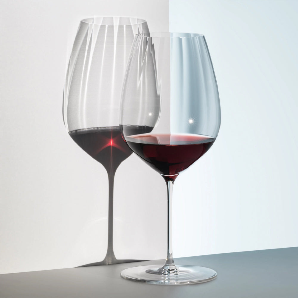 Transparent glass wine glass with red wine, light reflection on white and grey surface.