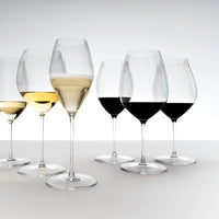 Set di sei calici trasparenti in vetro con vino rosso, bianco e spumante su superficie bianca e sfondo chiaro.