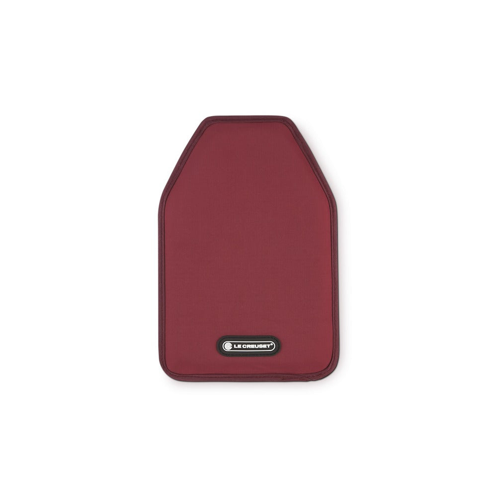 Sottopentola rettangolare in tessuto borgogna con bordo. Presente logo "LE CREUSET" in bianco su fondo nero. Sfondo bianco.