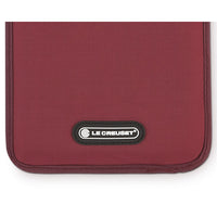 Burgundy fabric placemat with black "LE CREUSET" logo on the side.