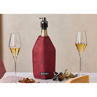 Wine bottle covered by a red case, next to two champagne glasses, a plate with dried fruit and a piece of cheese.