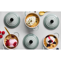 Beige and green ceramic bowls with desserts and ice cream, garnished with red berries, and golden spoon beside. Neutral setting.