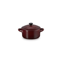 Round ceramic casserole red with black lid, side handles, on white background.