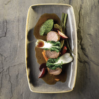 Plato elegante con carne en rodajas, verduras coloridas y salsa oscura en un cuenco gris. Ambiente minimalista y refinado.