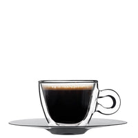 tazzina di caffè nero con schiuma in vetro trasparente su piattino rotondo grigio su sfondo bianco