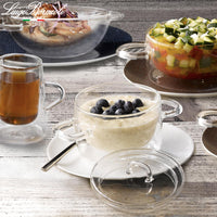 Transparante glazen kom met deksel, wit dessert met bosbessen, op wit bord, lichte houten achtergrond