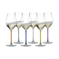 Set di sei calici di vino bianco con steli sottili colorati (arancione, verde, blu, trasparente, giallo, viola), su sfondo bianco.