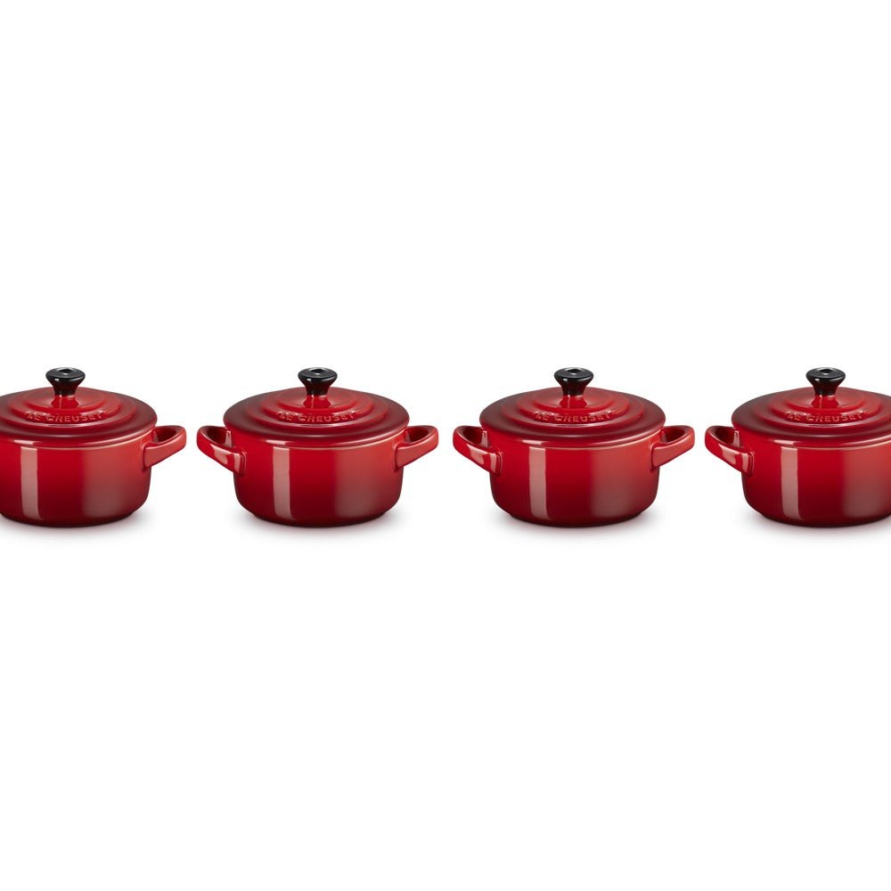 Set di quattro cocotte rotonde rosse in ceramica lucida, con coperchi neri e manici laterali.