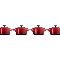 Quatre casseroles rouges en fonte, avec couvercle et poignées, alignées sur un fond blanc.