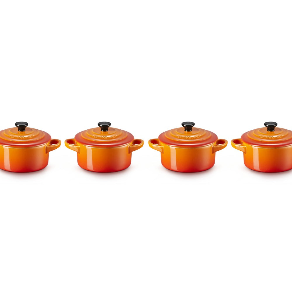 Set di quattro cocotte rotonde di colore arancione con tonalità sfumate, coperchi neri con pomello, in materiale ceramico lucido.