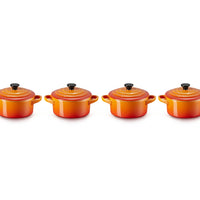 Set di quattro cocotte rotonde di colore arancione con tonalità sfumate, coperchi neri con pomello, in materiale ceramico lucido.