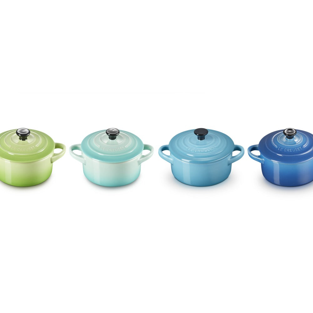 Set di quattro pentole in ceramica, nei toni del verde e blu, con coperchio e maniglie, su sfondo bianco.