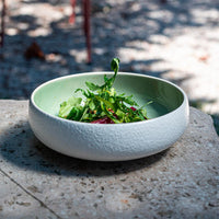 Ciotola tonda bianca esternamente e verde chiaro internamente in ceramica con insalata verde su superficie di pietra all'aperto.
