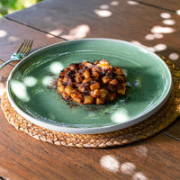 gnocchi di patate disposti a disco con salsa scura su piatto verde ceramica, posato su tovaglietta in fibra naturale su tavolo legno
