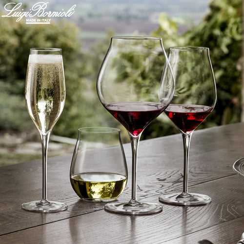 quattro bicchieri trasparenti di vetro di forme diverse con vino rosso, bianco e spumante su tavolo di legno