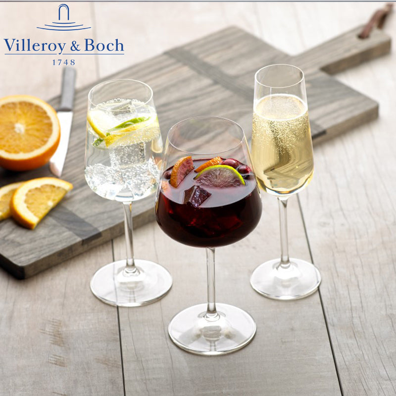 Tre bicchieri di vetro con bevande colorate su un tavolo in legno: un cocktail rosso, una bevanda frizzante e un drink dorato; arance affettate