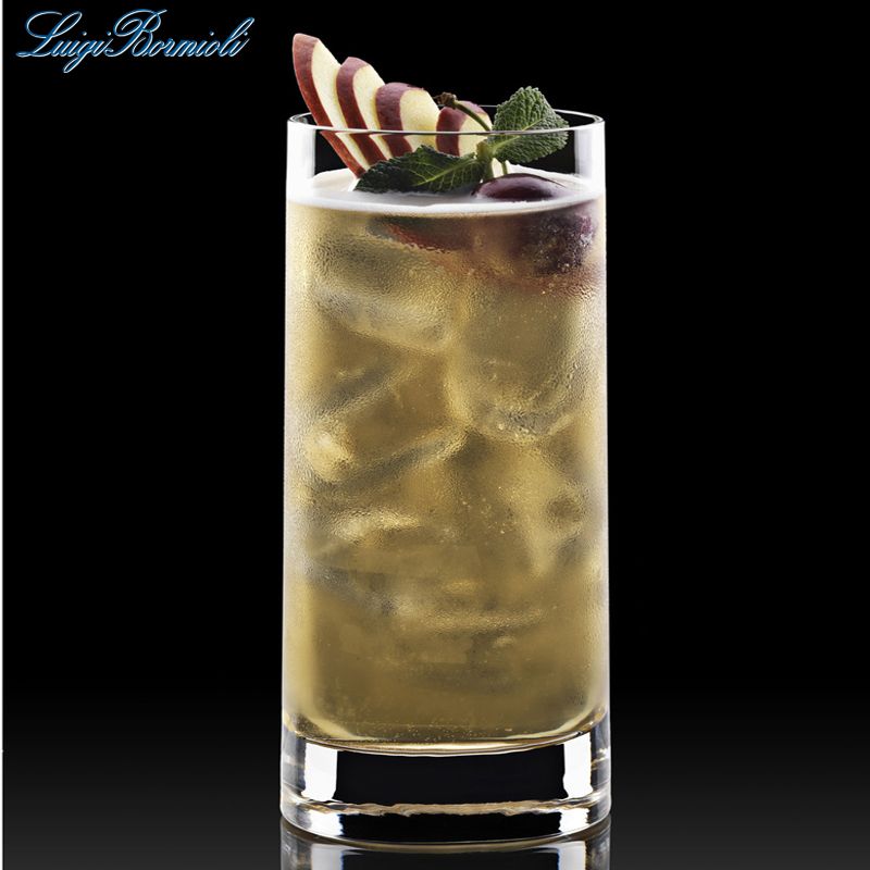 Grand verre transparent avec boisson jaune, glace et garniture de tranches de pomme, raisin et feuille de menthe