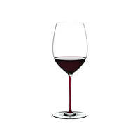 Calice di vino trasparente con stelo sottile, contenente vino rosso scuro, su sfondo bianco.