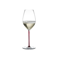 Copa de vino transparente con tallo rojo, que contiene un líquido espumoso de color claro. Fondo blanco.