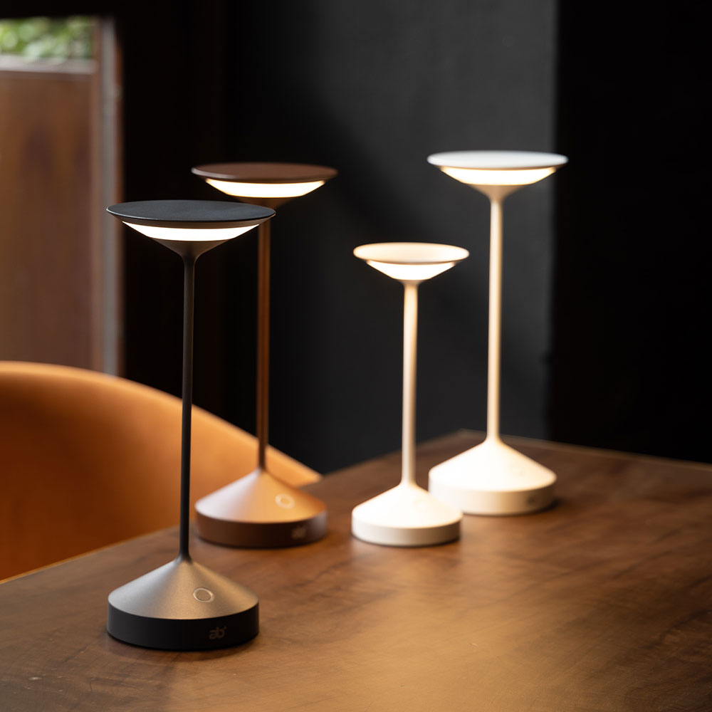 Four upside-down plate-shaped table lamps in metal and plastic, black, brown and white colours, on wooden table in setting