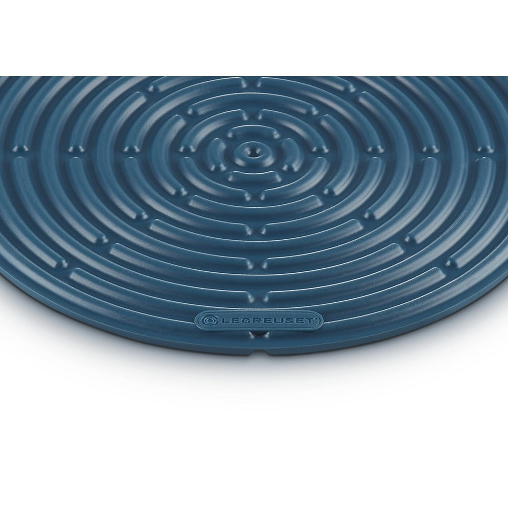 Tapis circulaire bleu foncé à motif spiralé, matériau apparemment en silicone, logo "LE CREUSET" visible.