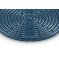Tapis circulaire bleu foncé à motif spiralé, matériau apparemment en silicone, logo "LE CREUSET" visible.