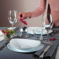 Set table with white plates, transparent glasses, silver cutlery and hand holding berries