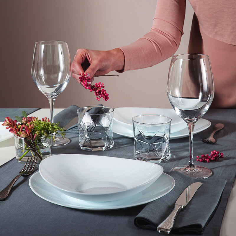 Set table with white plates, transparent glasses, silver cutlery and hand holding berries