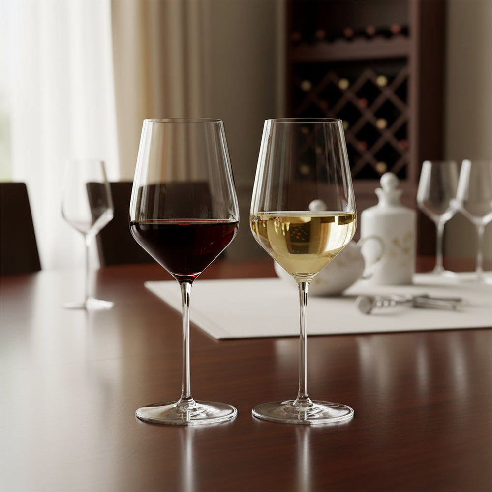 Dos calices de vidrio transparente con vino tinto y blanco sobre mesa de madera, fondo con botellero y otros calices vacíos.