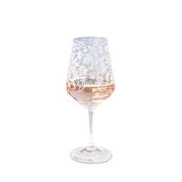 Clear glass wine glass with white marine element engravings, partially filled with rosé wine on white background
