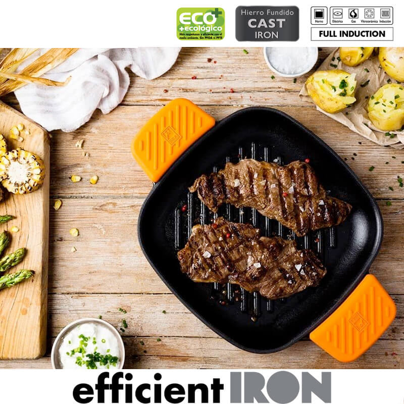 Poêle en fonte noire avec poignées orange, contient viande grillée et accompagnements d'asperges et maïs grillé sur table en bois.