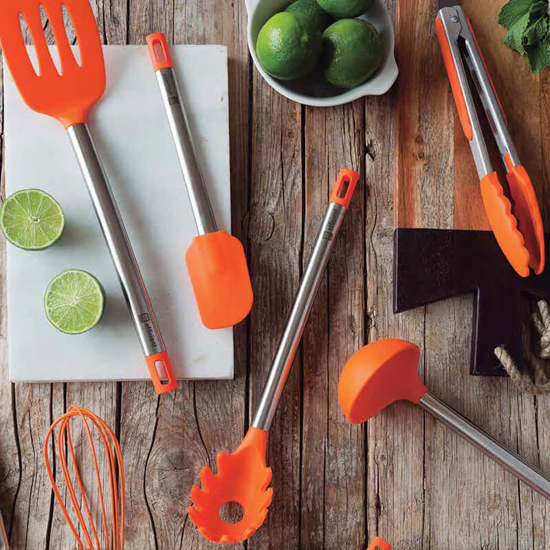 Utensili da cucina in acciaio inox con manici arancioni, lime a fette e una ciotola con limoni su un tavolo in legno.