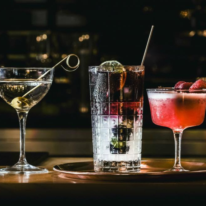 Tre cocktail su un vassoio: uno trasparente con oliva, uno alto con ghiaccio e lime, uno rosa con fragole