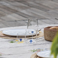 Table set with decorated light tablecloth, white plates on straw chargers, three transparent glass tumblers with blue spheres inside