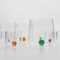 Transparent glass tumblers with colored orange, green, pink and blue beads inside on white surface