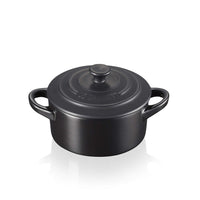 Matte black cast iron cocotte pot with two handles and lid with central knob, Le Creuset logo engraved on the lid.