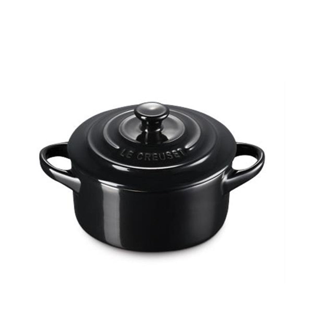 Round black enameled cocotte pot with two side handles and lid with central knob and LE CREUSET inscription on white background.