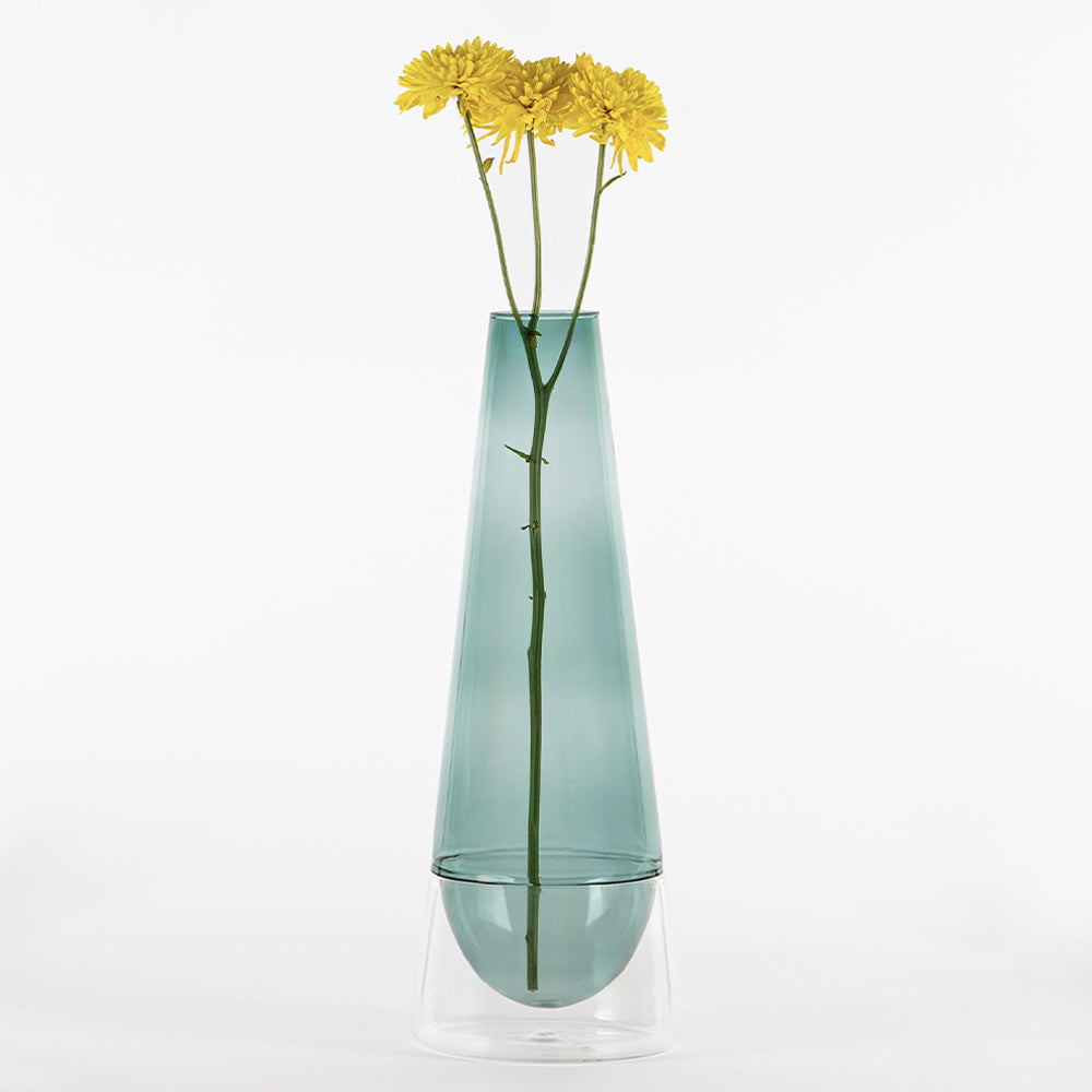 vase bleu clair transparent en verre avec base claire contenant trois fleurs jaunes à tiges vertes sur fond blanc