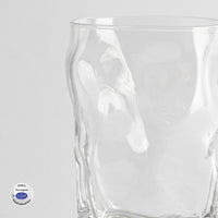 bicchiere di vetro trasparente con superficie irregolare e logo circolare bianco e blu sullo sfondo bianco