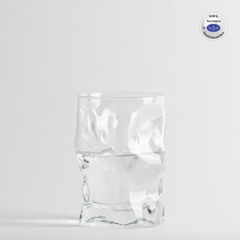 Bicchiere trasparente irregolare in vetro con acqua, sfondo bianco con etichetta cerchiata in alto a destra