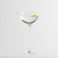 Calice en verre transparent avec boisson limpide et petite décoration jaune flottante sur fond blanc