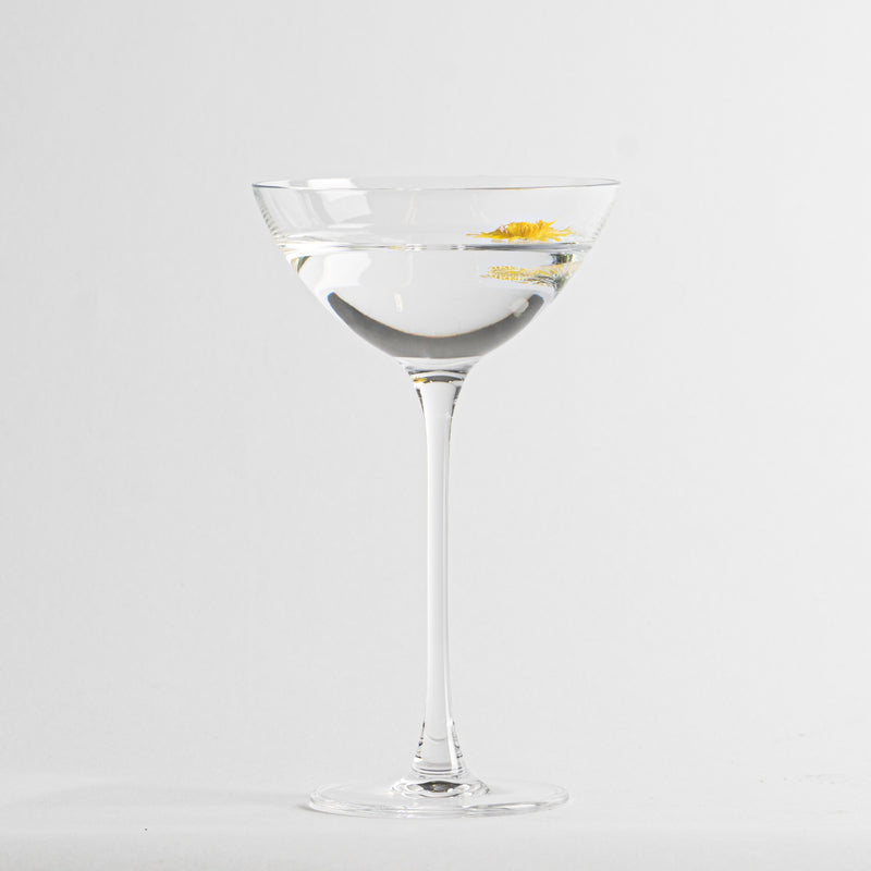 Calice en verre transparent avec boisson limpide et petite décoration jaune flottante sur fond blanc